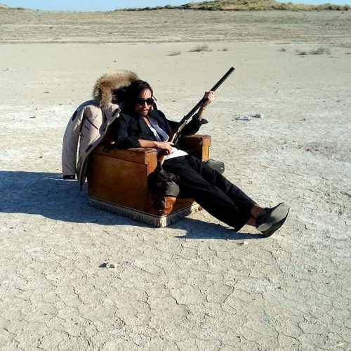Persona sentada en un sofa en el desierto con una escopeta